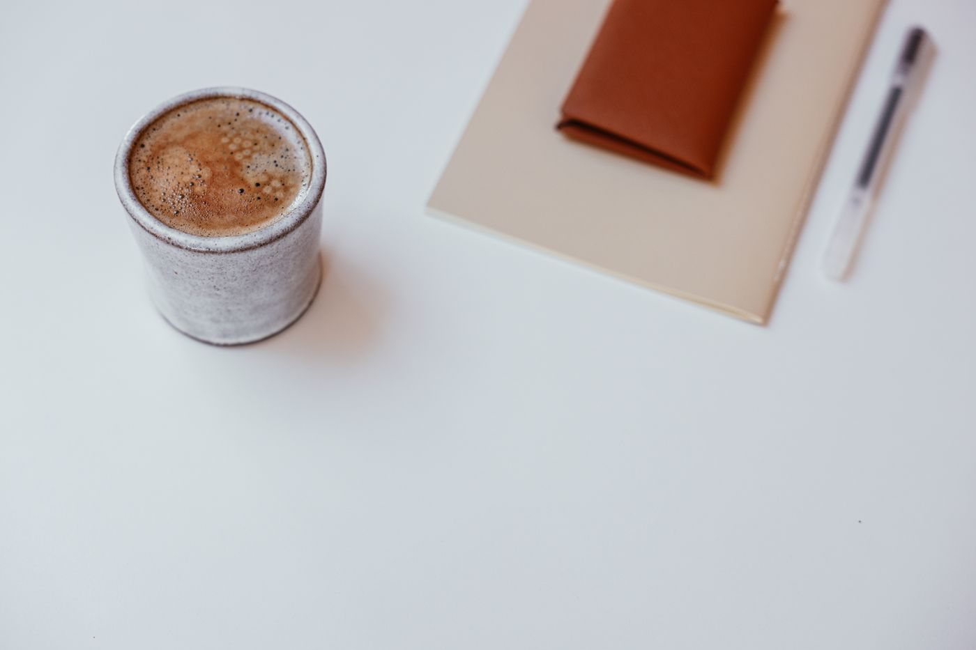 白いテーブルに置かれたコーヒーと、ノートとペン