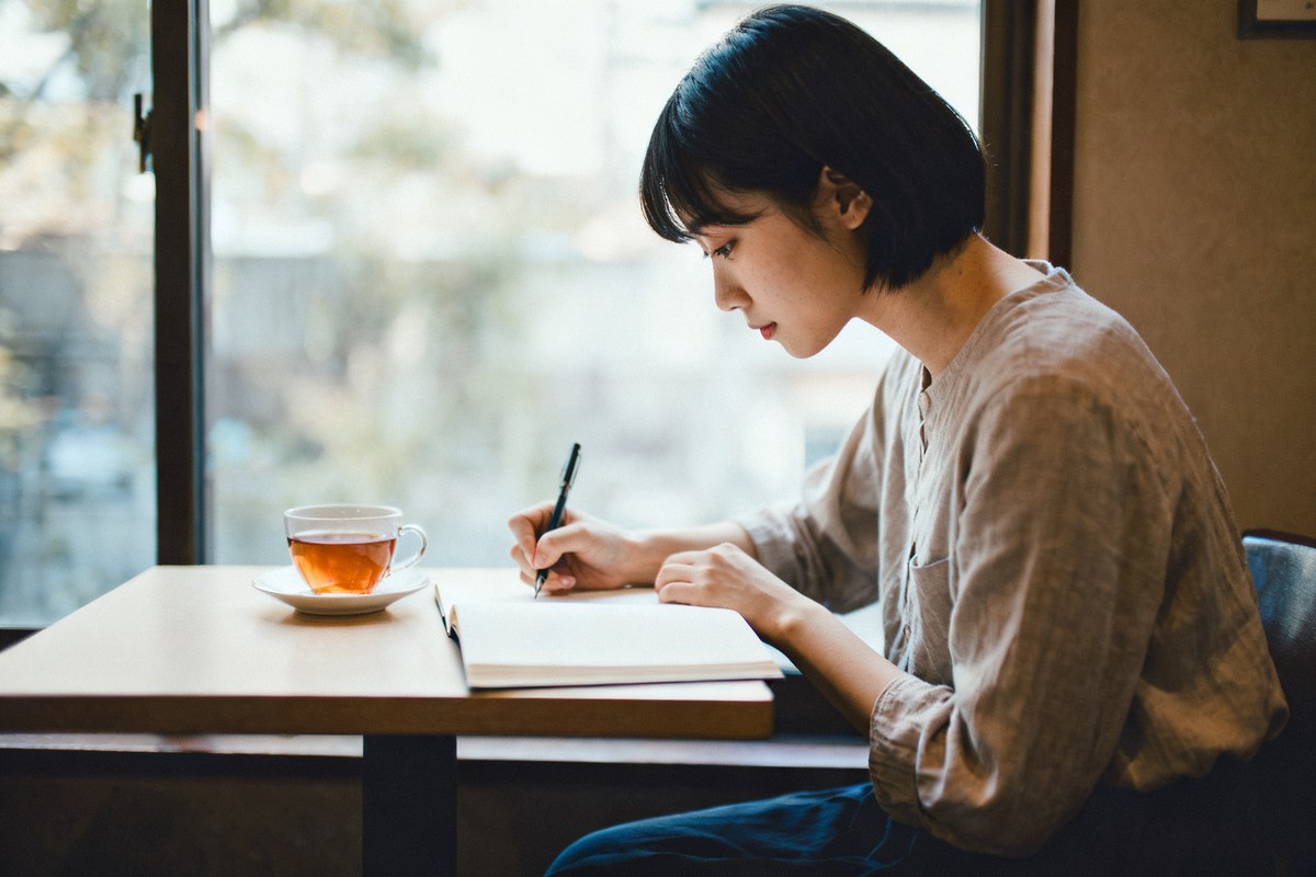 カフェの窓際で、ノートにこれまでの活動を書き出していく女性