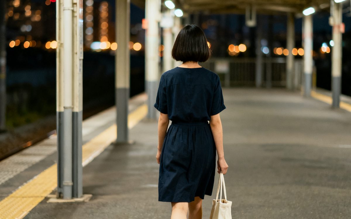 夜の駅のホームを、ひとりで歩いていく女性の後ろ姿