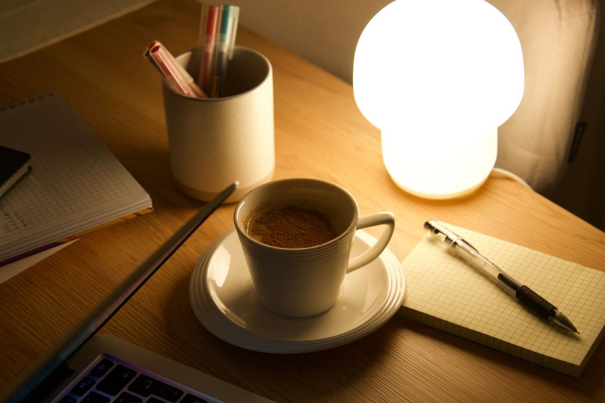 夜、明かりをつけた机に置かれたノートパソコンとコーヒー