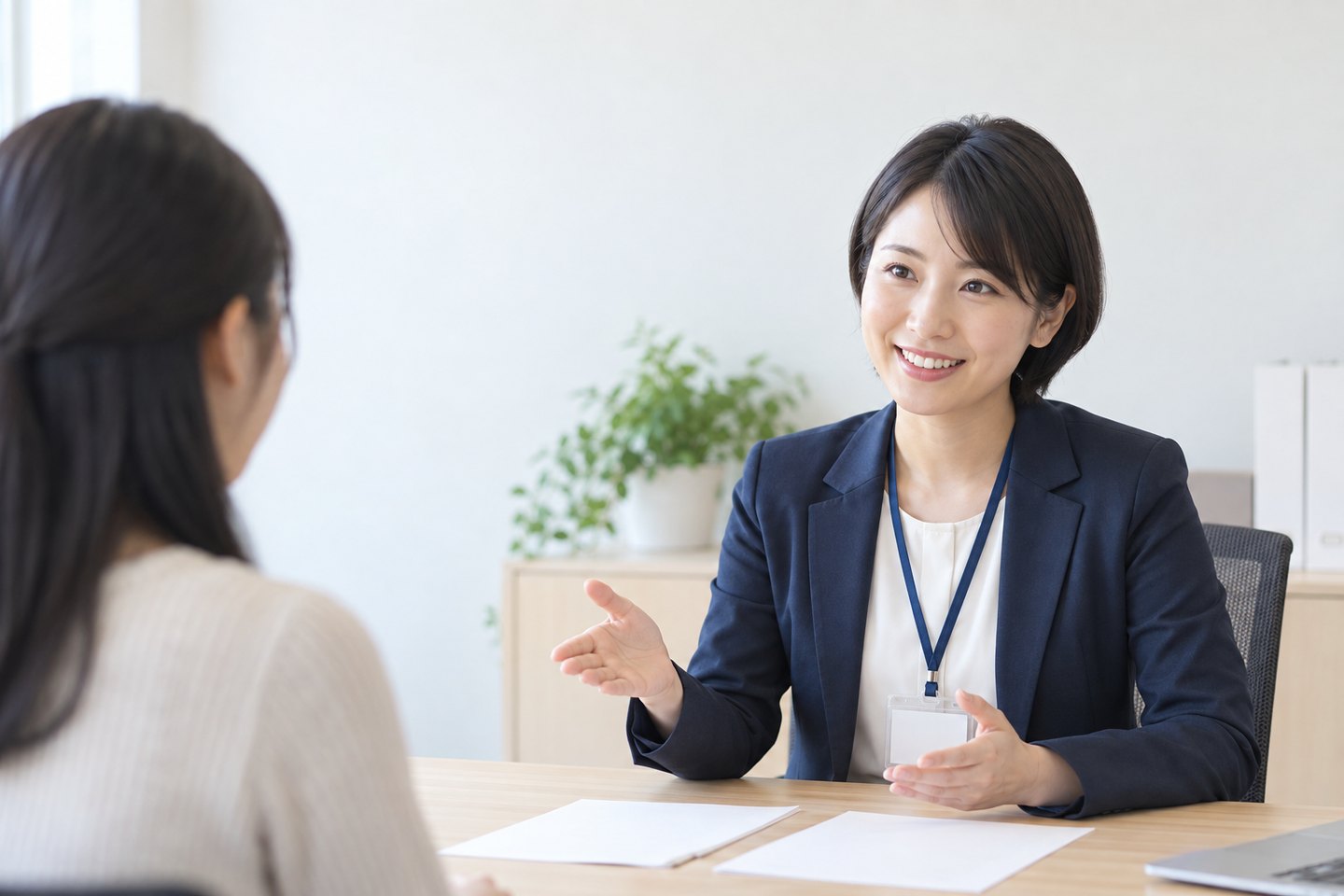 相談の席で、スーツ姿のアドバイザーが、向かいに座る女性に笑顔で話している