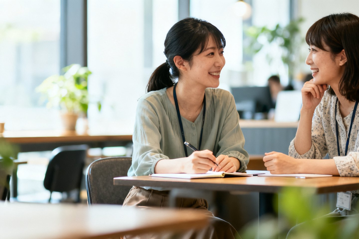 明るいオフィスで、ノートを開いて笑顔で話をしている二人の女性