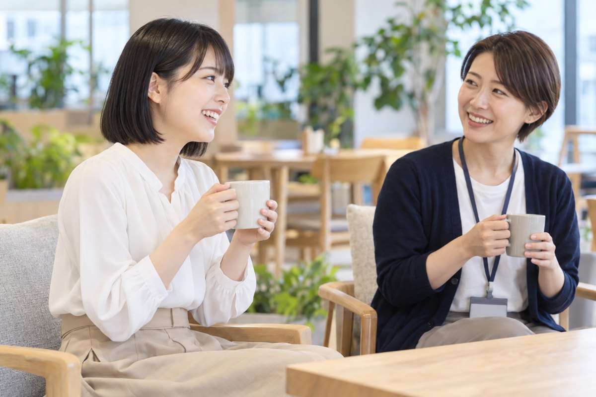 オフィスの休憩スペースで、入社したばかりの女性と先輩の女性がコーヒーを手に笑顔で話している